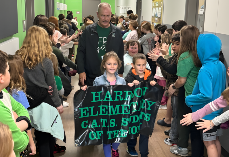 Kids holding sign with people walking behind and other students standing on sides